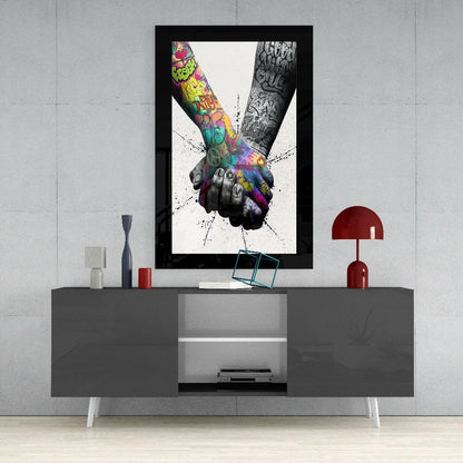 Framed artwork displaying two tattooed arms joining hands with colorful graffiti and black ink designs against white background, mounted above gray media console.