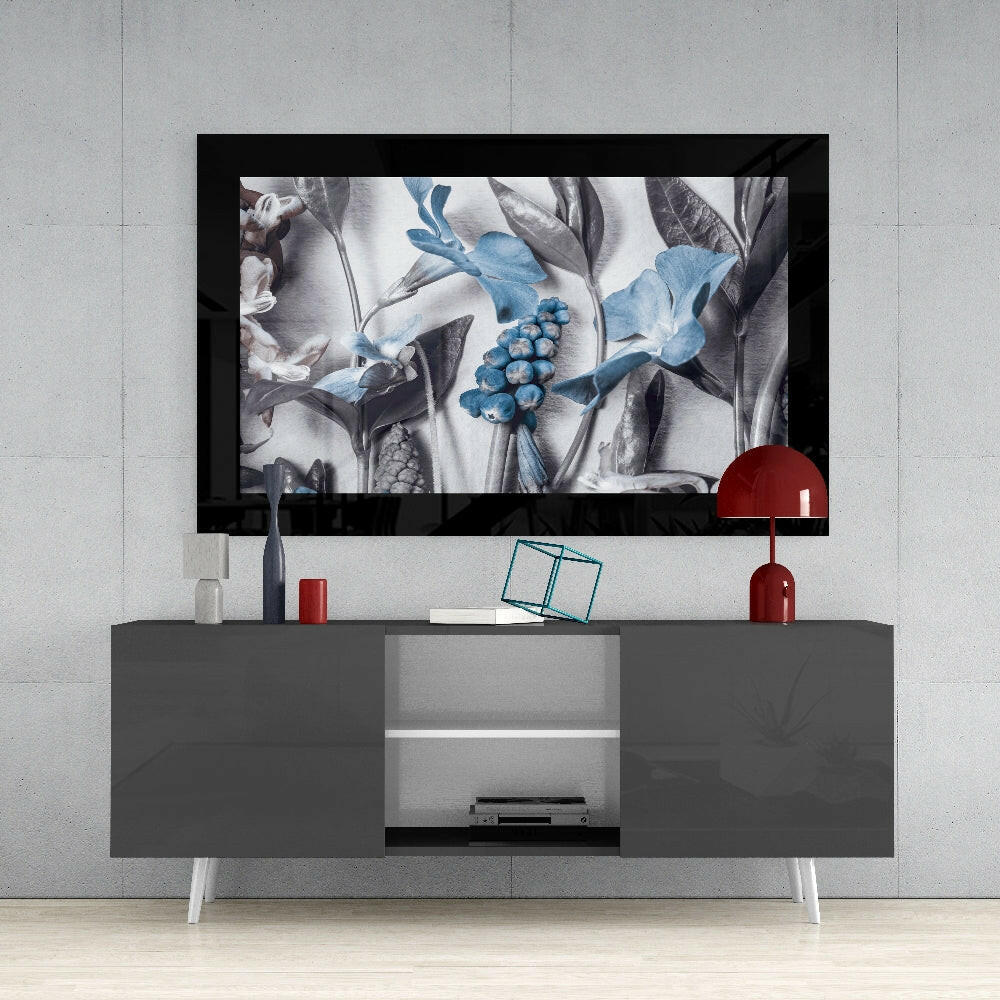 Framed botanical glass art displaying blue flowers and gray foliage displayed above gray media console in modern interior setting.