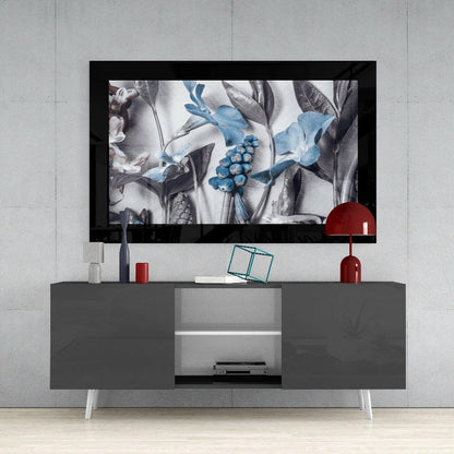 Framed botanical glass art displaying blue flowers and gray foliage displayed above gray media console in modern interior setting.