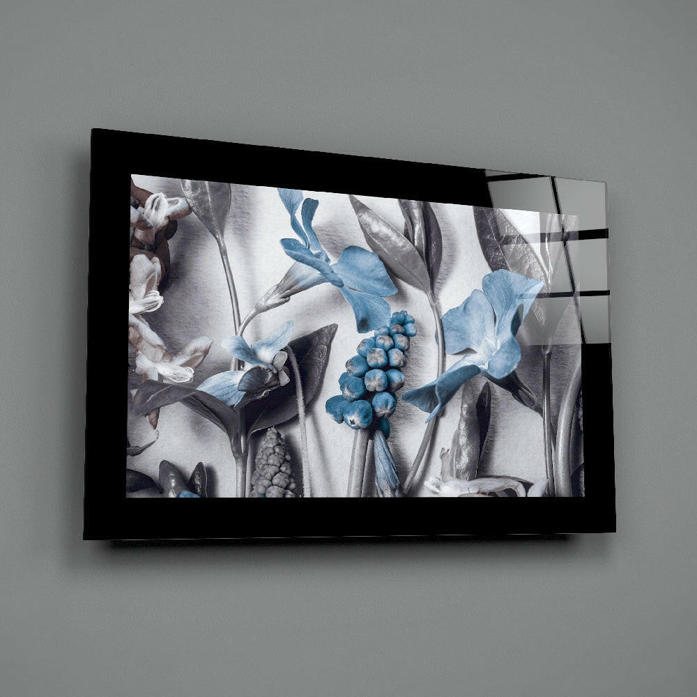 Black-framed glass wall art displaying botanical illustration with blue flowers, berries, and gray foliage against white background, mounted on gray wall.