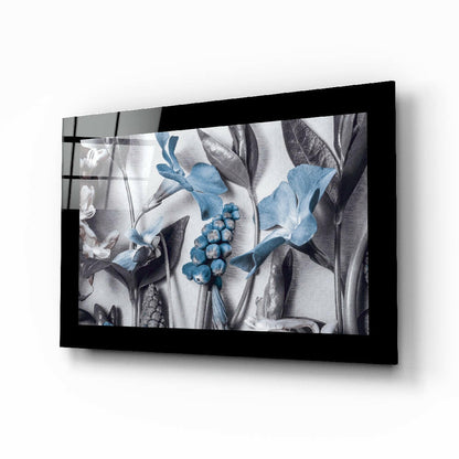 Black-framed glass wall art displaying botanical illustration with blue flowers, berries, and grayscale leaves mounted at angle.