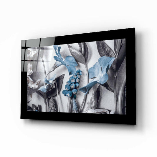 Black-framed glass wall art displaying botanical illustration with blue flowers, berries, and grayscale leaves mounted at angle.