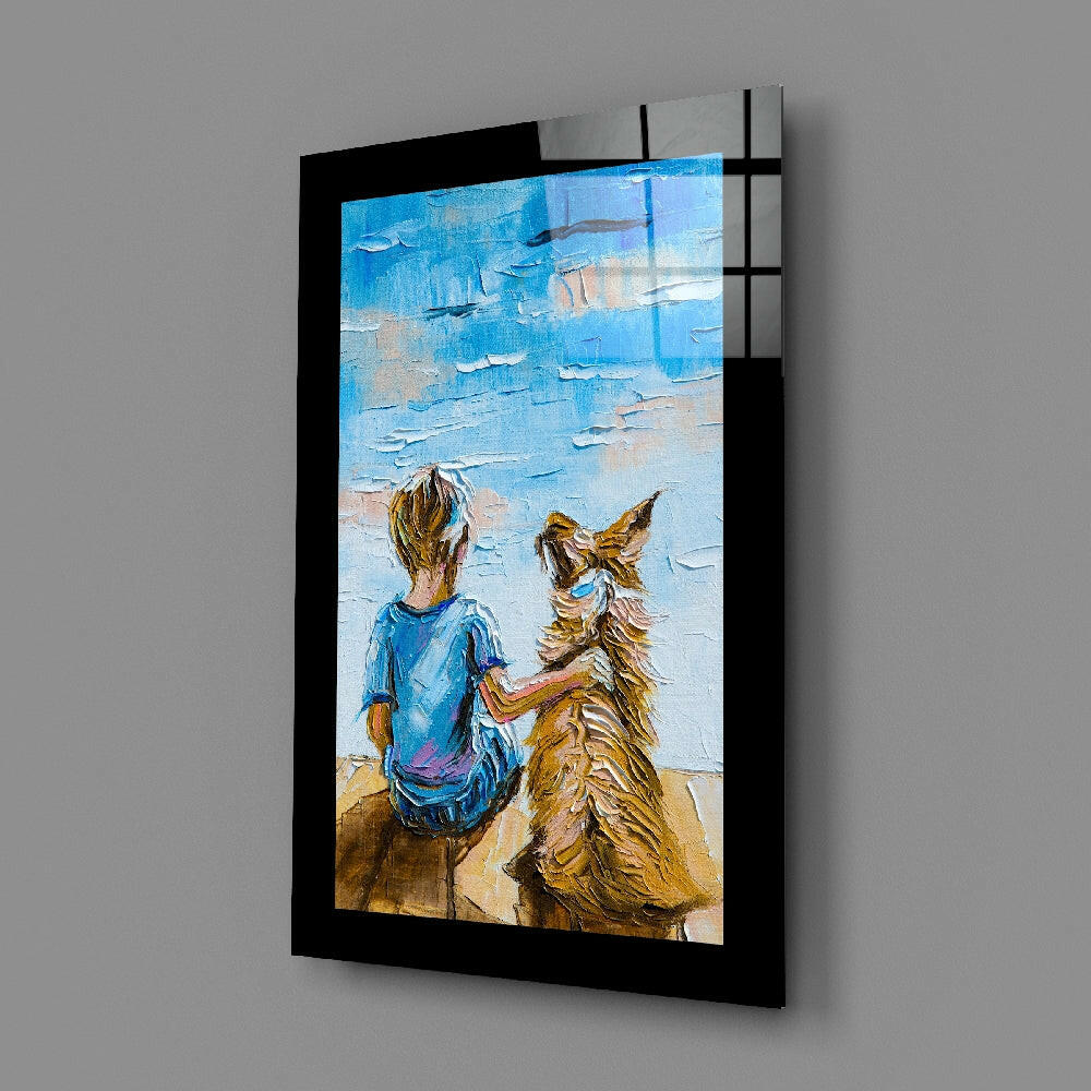 Black-framed glass wall art displaying a child in blue shirt and brown dog sitting on beach facing blue ocean, angled perspective view.