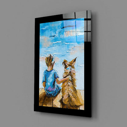 Black-framed glass wall art displaying a child in blue shirt and brown dog sitting on beach facing blue ocean, angled perspective view.