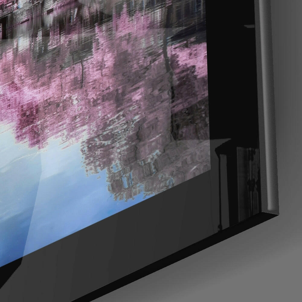 Angled side view of glass wall art displaying pink cherry blossoms and blue sky reflection on black frame.