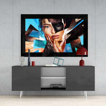 Modern glass wall art displaying an abstract portrait of a woman's face with geometric blue, orange, and earth-tone overlays mounted above a gray media console.