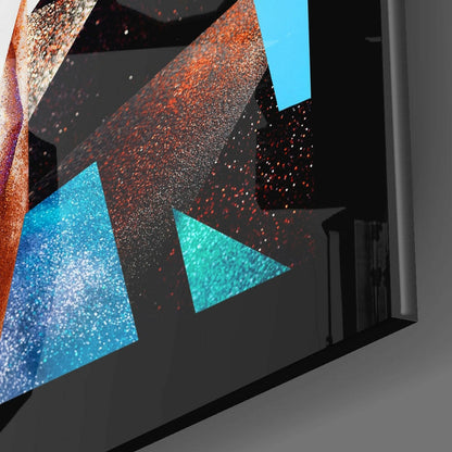 Close-up angled view of modern glass wall art featuring blue and orange glittery triangular shapes on black background.