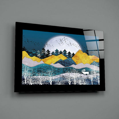 Black-framed glass wall art displaying layered landscape with full moon, golden mountains, evergreen trees, white birches, and grazing deer against blue sky.