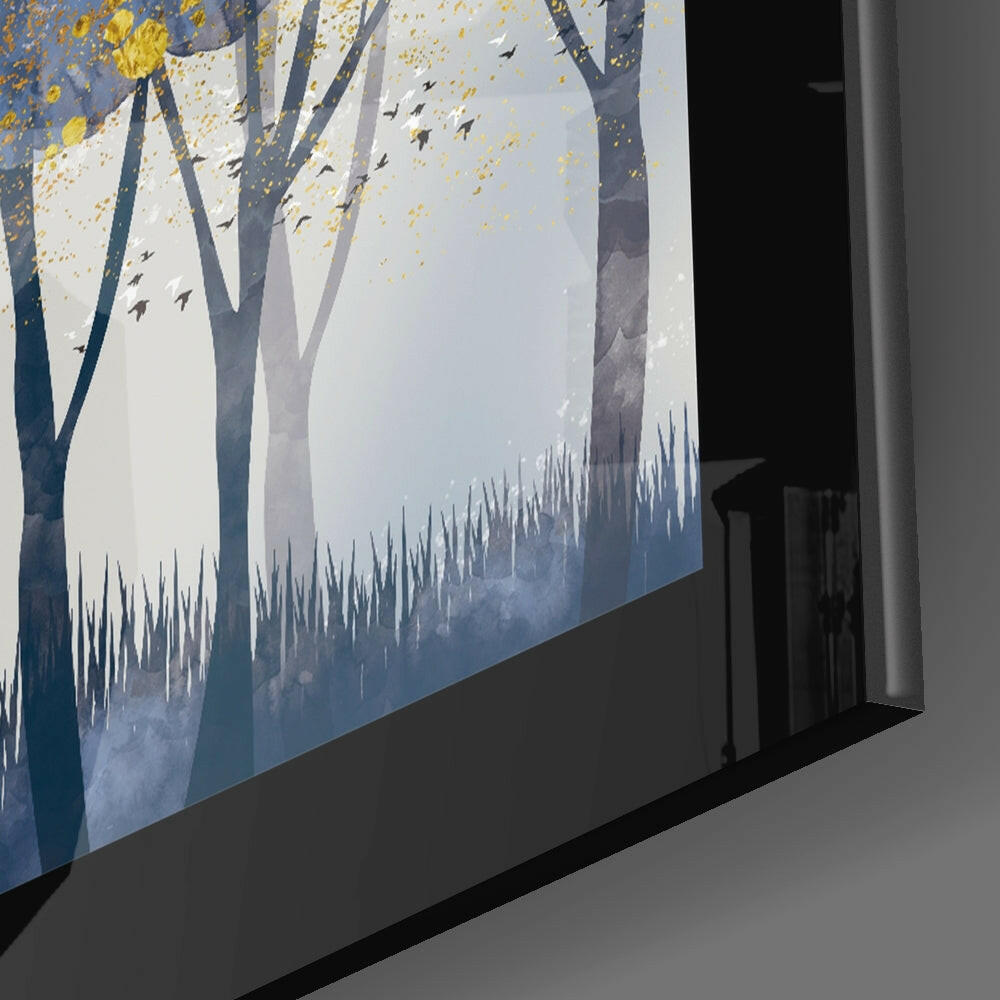 Angled view of glass wall art displaying stylized forest scene with blue-gray trees, golden foliage, flying birds, and misty landscape against white background.