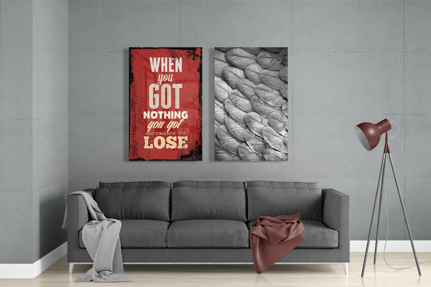 Modern living room with gray sofa displaying two glass wall art panels: red motivational text panel and monochrome feather pattern panel.