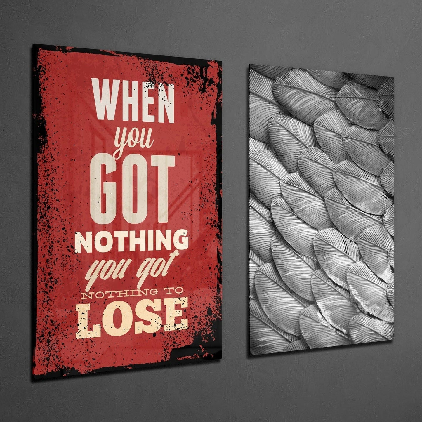 Two glass wall art panels mounted on gray wall: left panel red with distressed edges and cream text reading "When you Got Nothing you got Nothing to Lose"; right panel black and white feather pattern design.