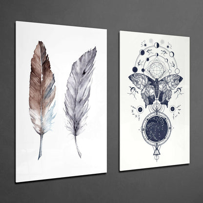Two framed glass wall art pieces displayed at an angle: left panel shows two watercolor feathers in brown and gray tones; right panel features an intricate black ink illustration of a moth with celestial and geometric symbols.