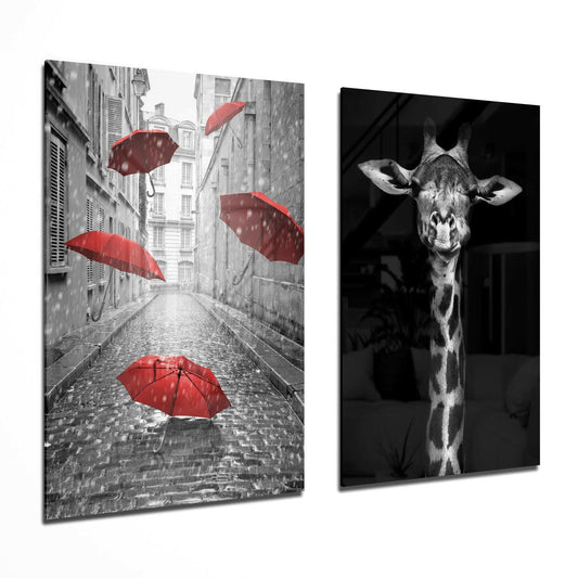 Two glass wall art panels displayed at an angle: left panel shows a rainy Paris street with red umbrellas in black and white; right panel features a black and white giraffe portrait.
