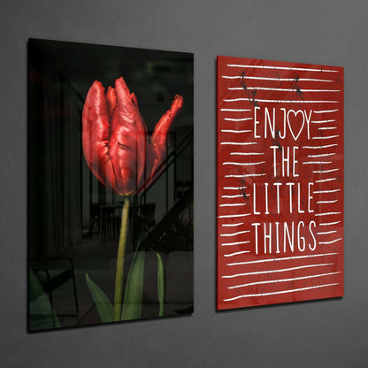 Two framed glass wall art pieces mounted on gray wall: left panel shows red tulip with green stem on dark background; right panel displays red background with white text reading "ENJOY THE LITTLE THINGS" in horizontal lines.