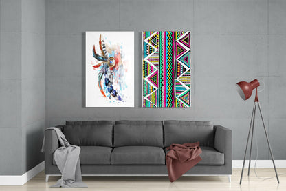 Two framed glass artworks displayed above a gray sofa: left panel shows watercolor feathers, right panel features geometric tribal patterns in bright colors.