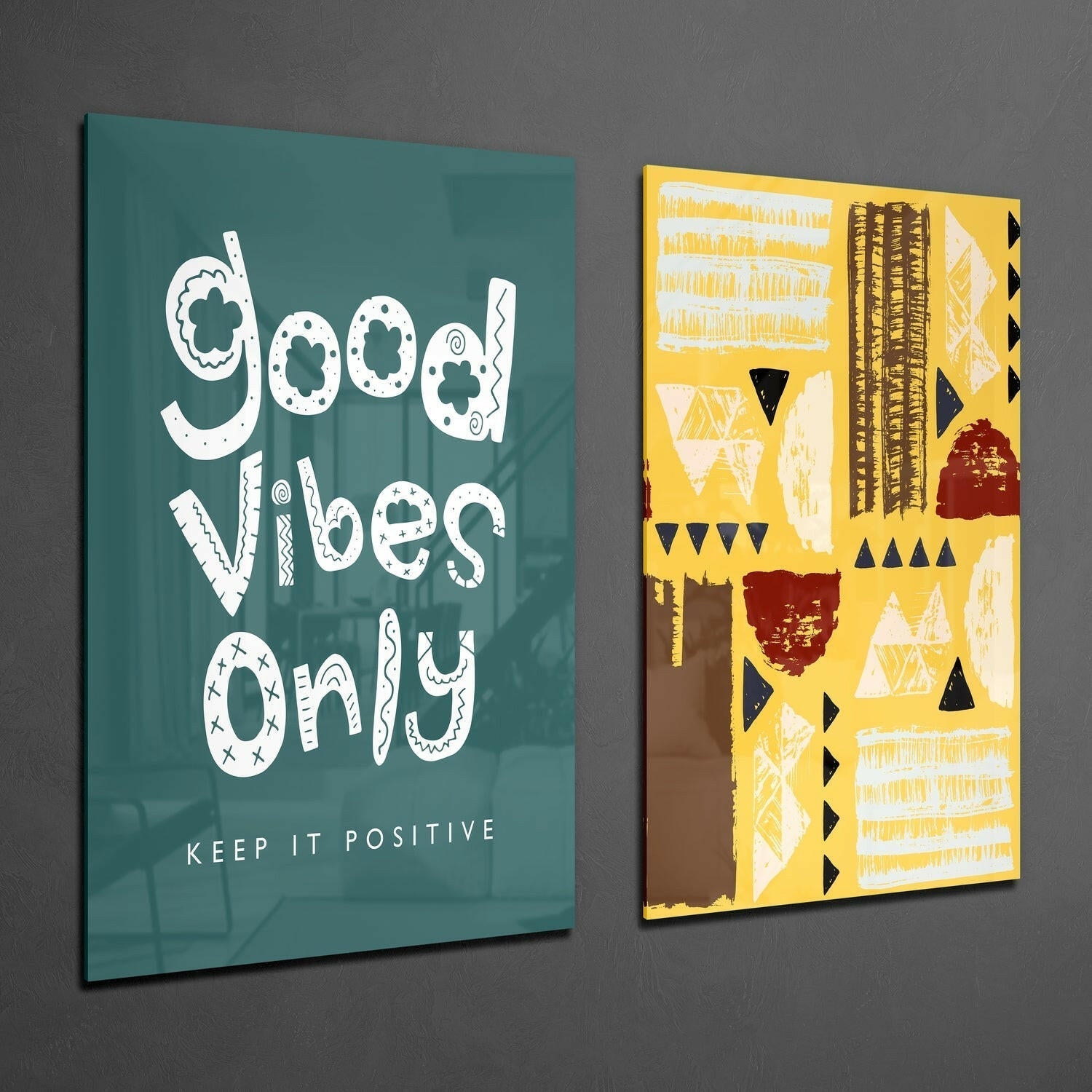 Two framed glass wall art pieces displayed at an angle against gray wall: left panel teal with white decorative text "Good Vibes Only" and "Keep It Positive"; right panel yellow with geometric patterns in black, white, and burgundy.