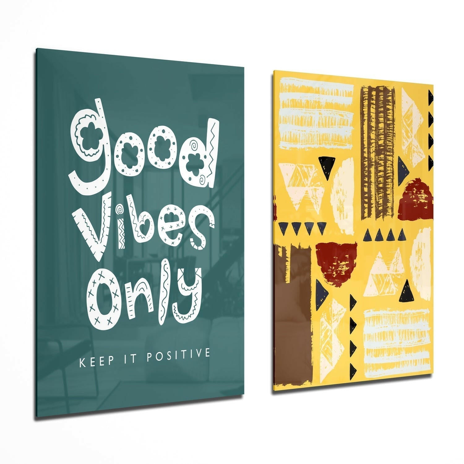 Two glass wall art panels displayed at an angle: one teal with white "Good Vibes Only" text, one yellow with geometric patterns in black, white, and red.