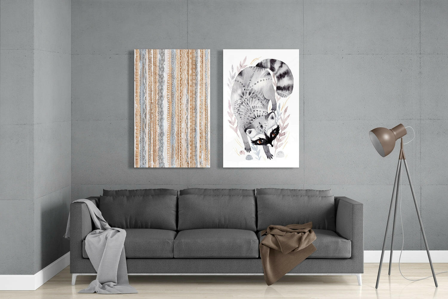 Two framed glass wall art pieces hanging above a gray sofa: left panel shows tan and blue geometric striped pattern; right panel depicts detailed black and white raccoon illustration with foliage.