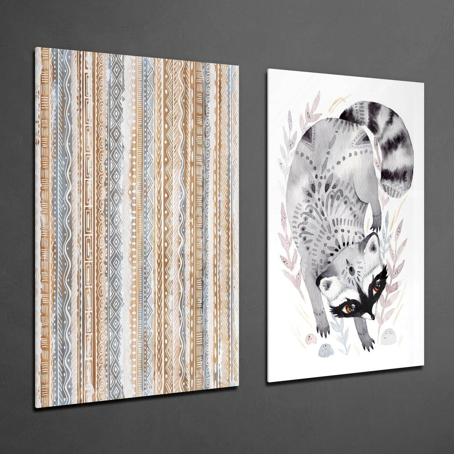 Two glass wall art panels displayed at an angle against gray wall: geometric striped pattern on left, illustrated raccoon with orange eyes and foliage on right.