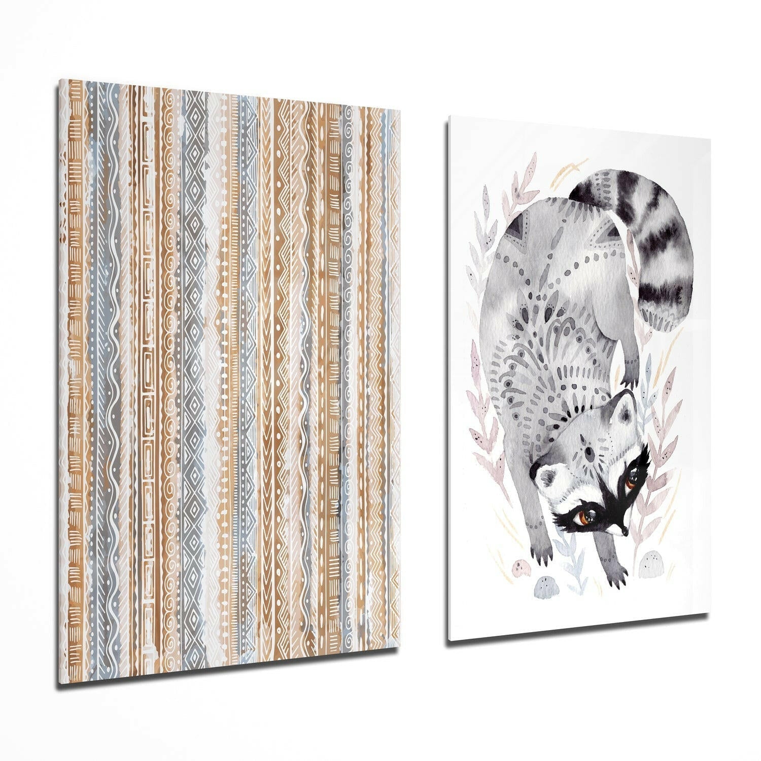 Two glass wall art panels displayed at an angle: left panel shows tan and gray geometric tribal stripes; right panel depicts a watercolor raccoon with striped tail among botanical elements.