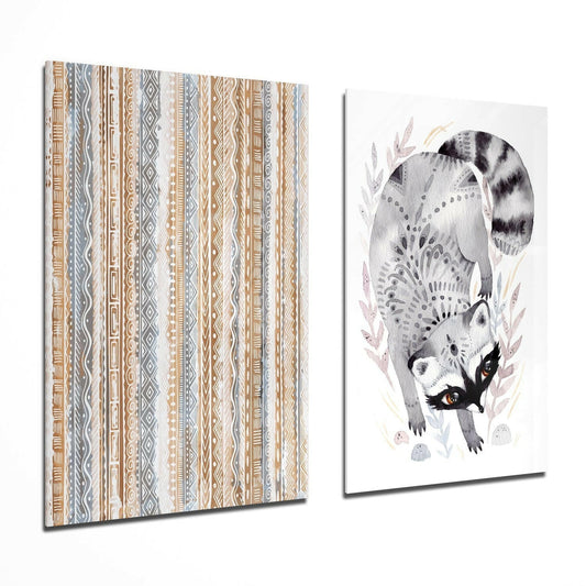 Two glass wall art panels displayed at an angle: left panel shows tan and gray geometric tribal stripes; right panel depicts a watercolor raccoon with striped tail among botanical elements.