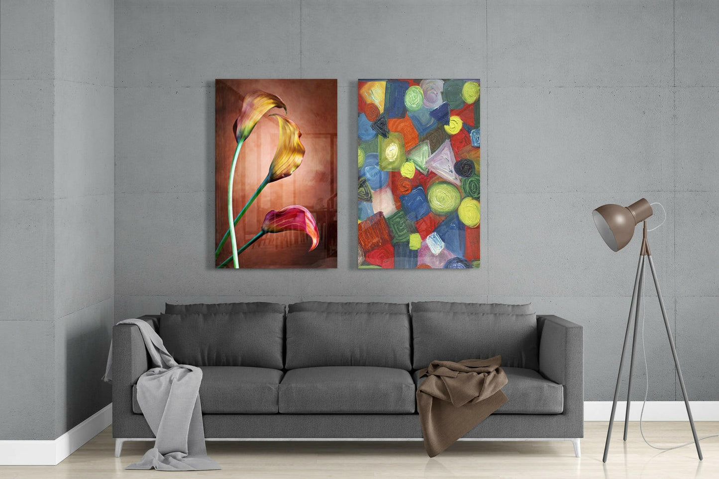 Modern living room with gray sofa displaying two glass wall art panels: golden tulips on warm background and colorful geometric shapes in bright hues.