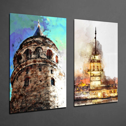 Two glass wall art panels displaying watercolor paintings of Istanbul's Galata Tower and Maiden's Tower against gray wall.