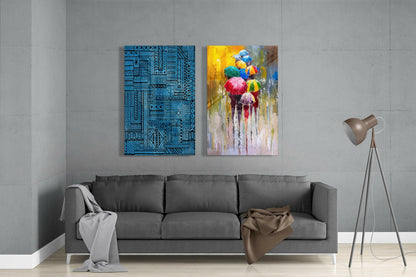 Modern living room with gray sofa displaying two glass wall artworks: geometric blue pattern and colorful umbrellas in rain scene.