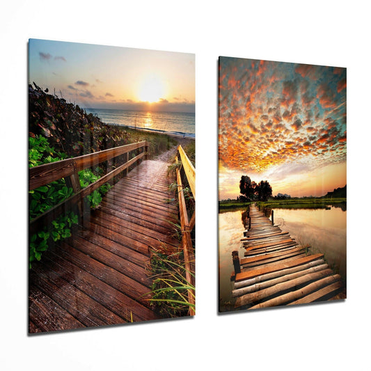 Two glass wall art panels displaying wooden boardwalks extending toward sunsets over water, with orange and golden sky reflections.