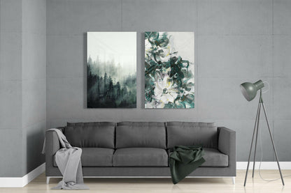 Modern living room interior with gray sofa displaying two glass wall art pieces: misty forest landscape and botanical floral design in green tones.