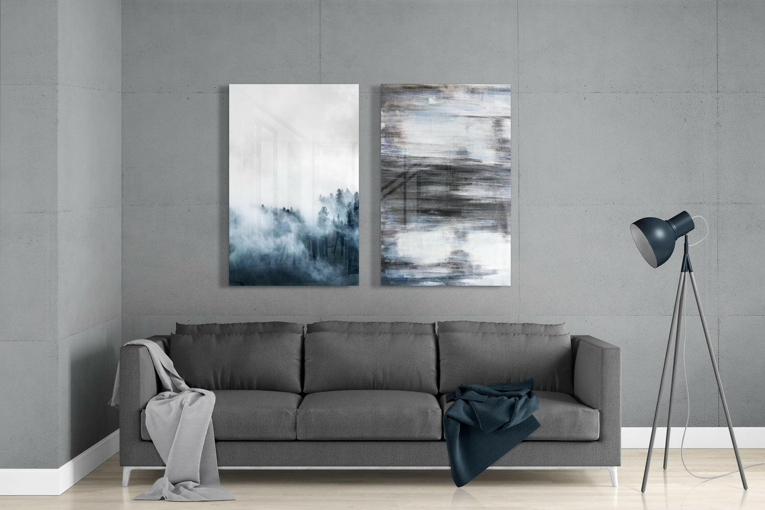 Gray sofa against concrete wall with two abstract glass artworks featuring forest and blue brushstroke designs above.