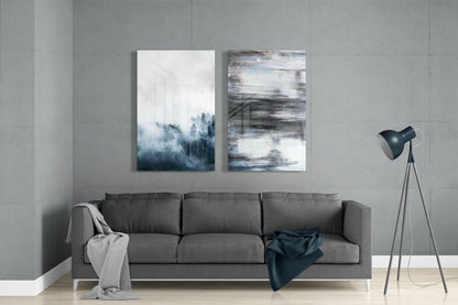 Gray sofa against concrete wall with two abstract glass artworks featuring forest and blue brushstroke designs above.