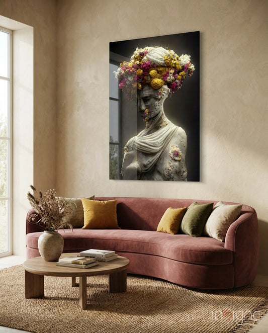 Glass wall art depicting a classical stone bust adorned with vibrant yellow, pink, and white flowers, displayed above a mauve sofa in a living room setting.