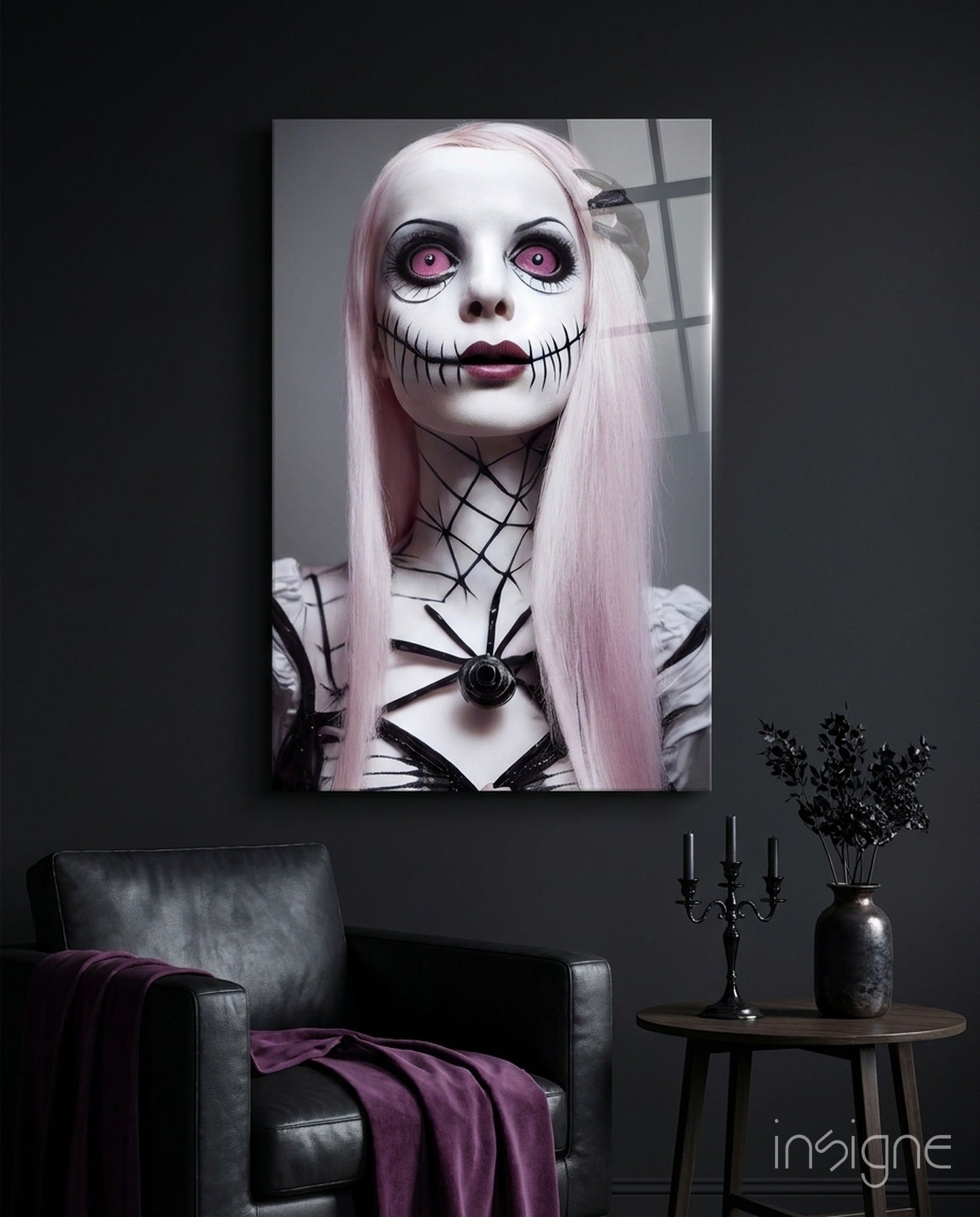 Glass wall art print depicting a pale-faced figure with pink eyes and stitched mouth, displayed above a black leather chair with purple fabric.