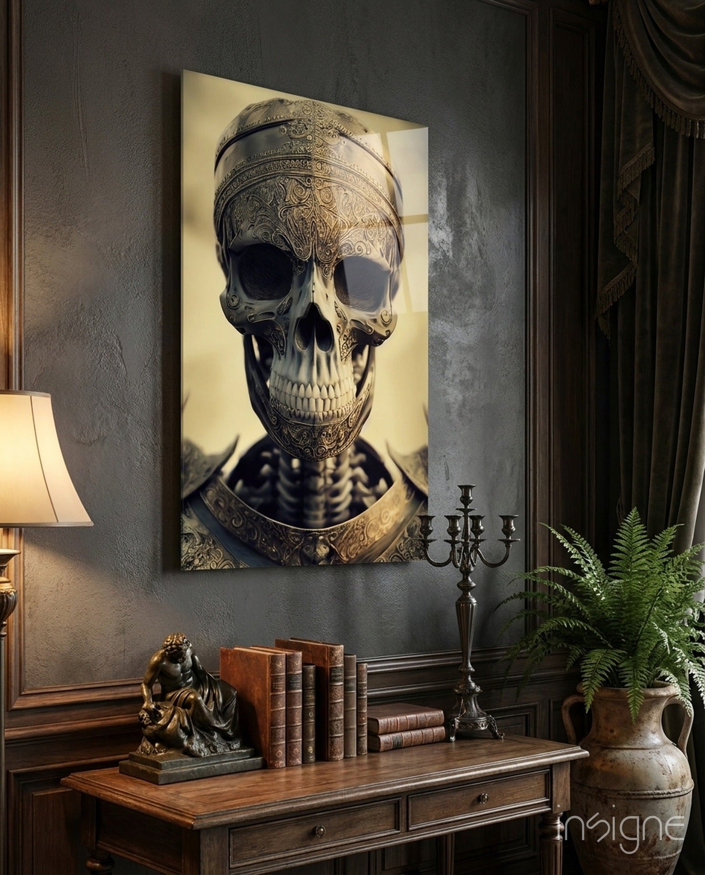 Ornate skull artwork with gold filigree detailing and cream background displayed above wooden desk with books and candelabra.