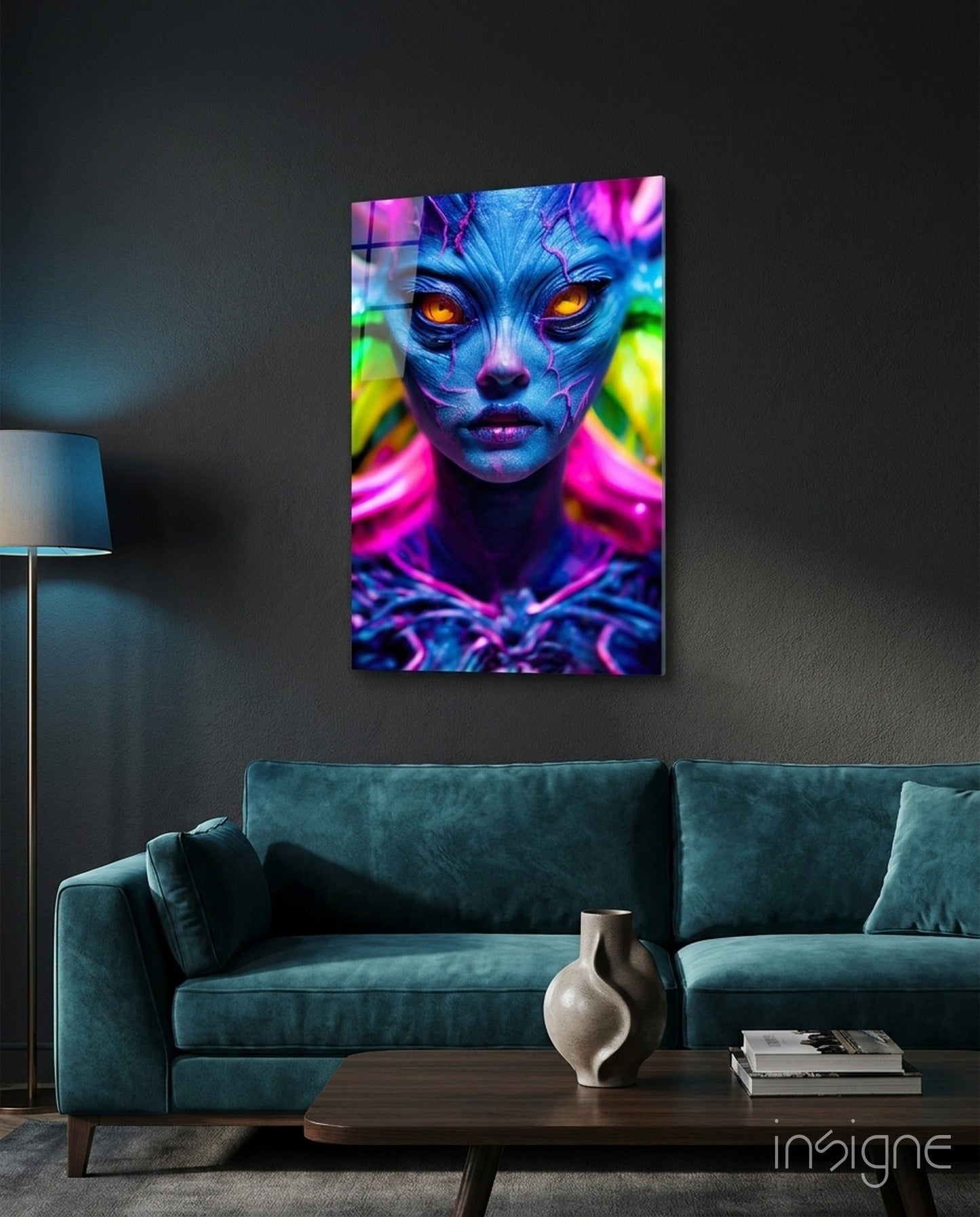 Vibrant neon portrait glass wall art displaying blue alien face with glowing orange eyes and magenta accents, mounted above teal sofa.