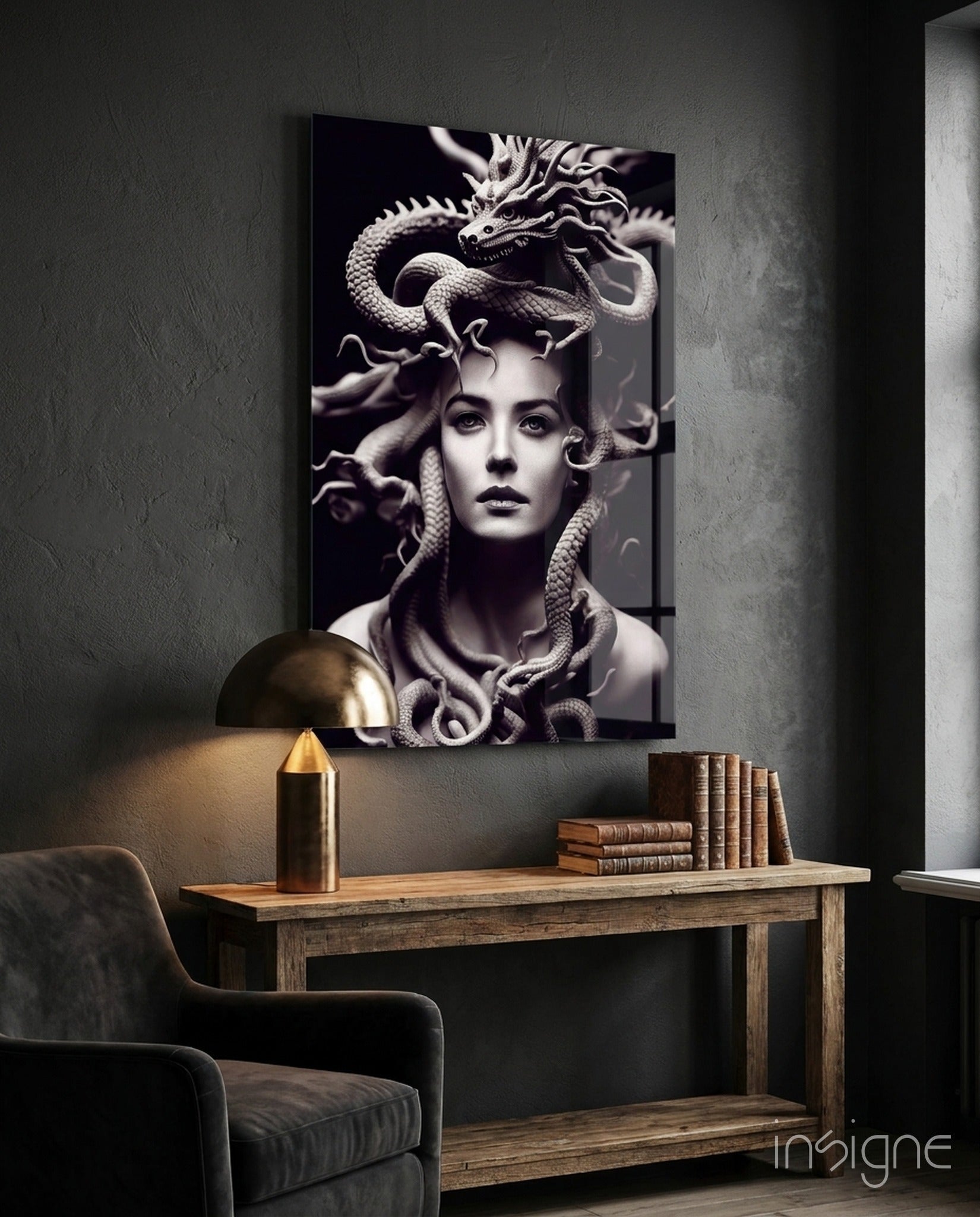 Monochromatic glass artwork depicting a woman's face with serpents and a dragon, mounted on a dark textured wall above a wooden desk.