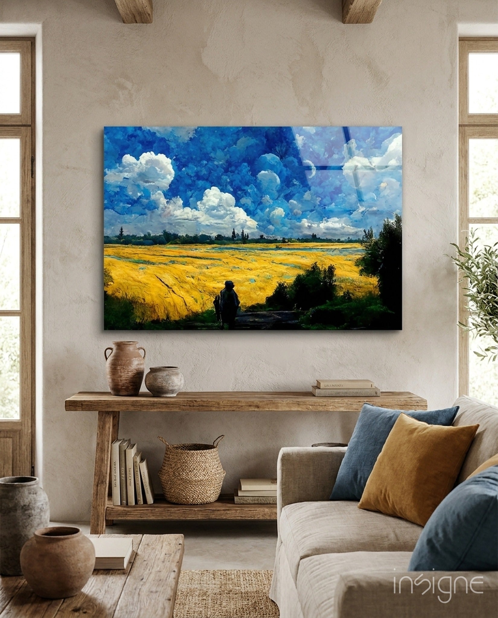 Glass art panel mounted on cream wall above wooden shelf, depicting yellow wheat field under blue sky with white clouds and solitary figure.