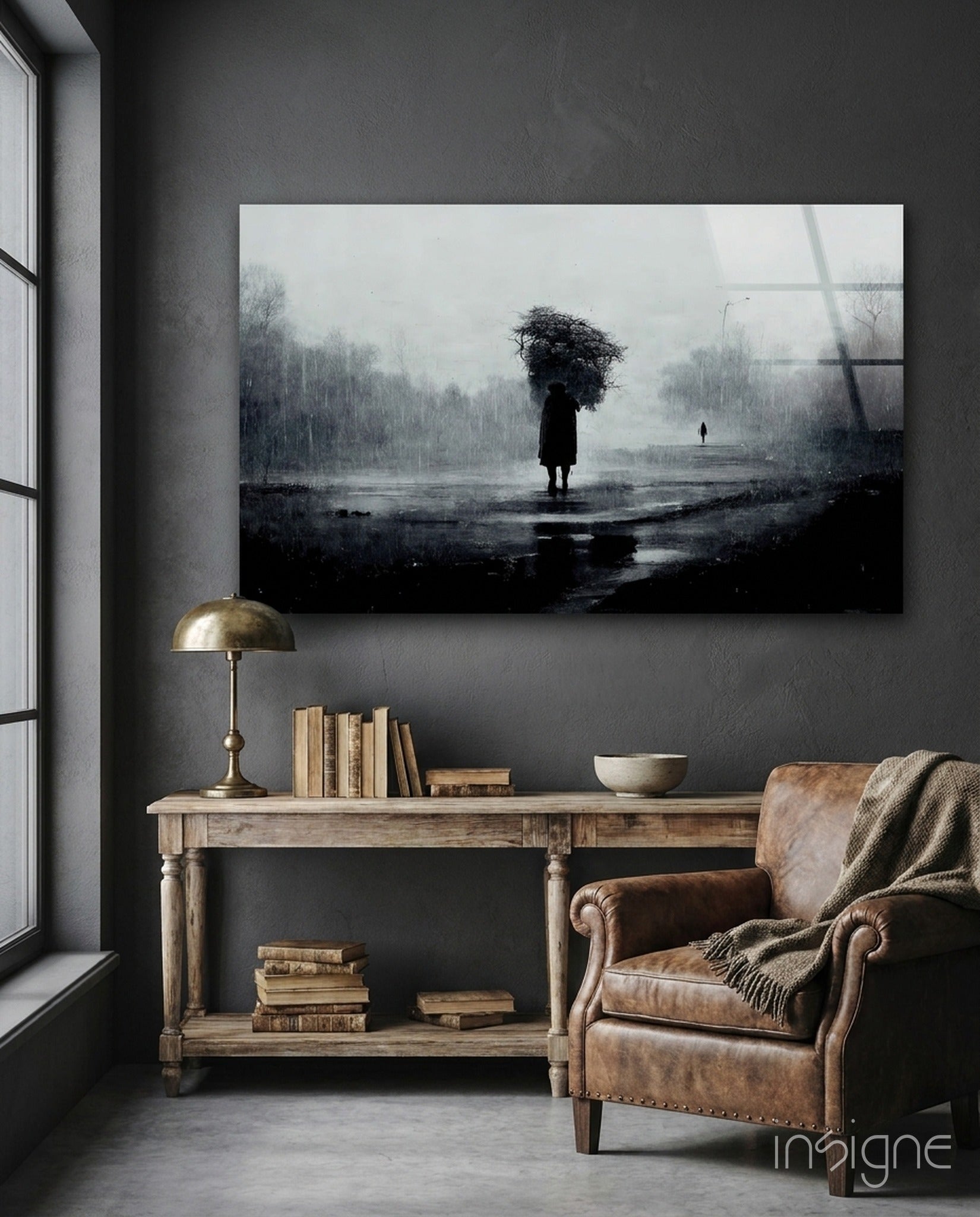 Moody black and white glass art depicting solitary figure with umbrella in rainy landscape, displayed above wooden console table in gray interior.