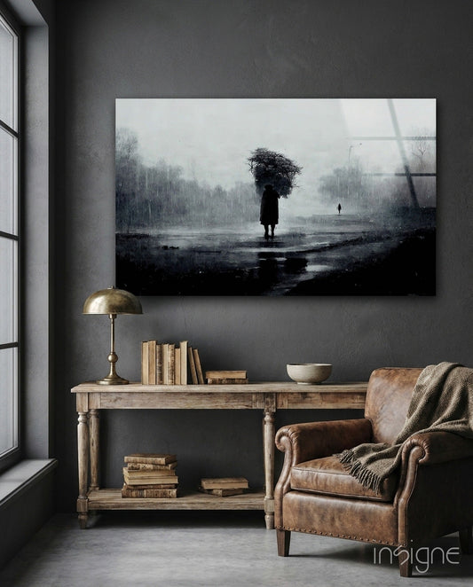 Moody black and white glass art depicting solitary figure with umbrella in rainy landscape, displayed above wooden console table in gray interior.