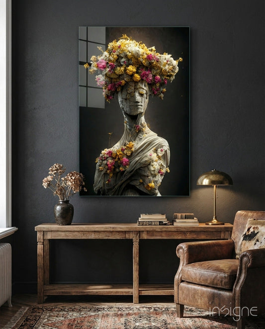 Stone bust with cascading dried flowers in gold, pink, and cream tones displayed above wooden desk in modern interior.