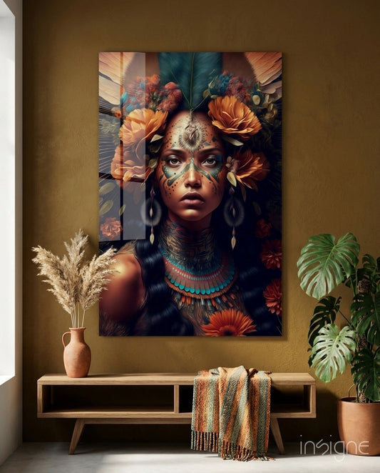 Glass wall art depicting a woman with face paint and orange flowers, displayed above a wooden console table with pampas grass and plants in a warm-toned room.