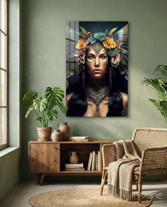 Glass wall art depicting a woman with facial tattoos and colorful flower headdress displayed above wooden furniture in a sage green room.