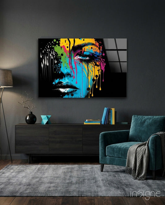 Colorful pop art portrait with cyan, yellow, and magenta paint drips displayed on dark wall above teal armchair and console table.