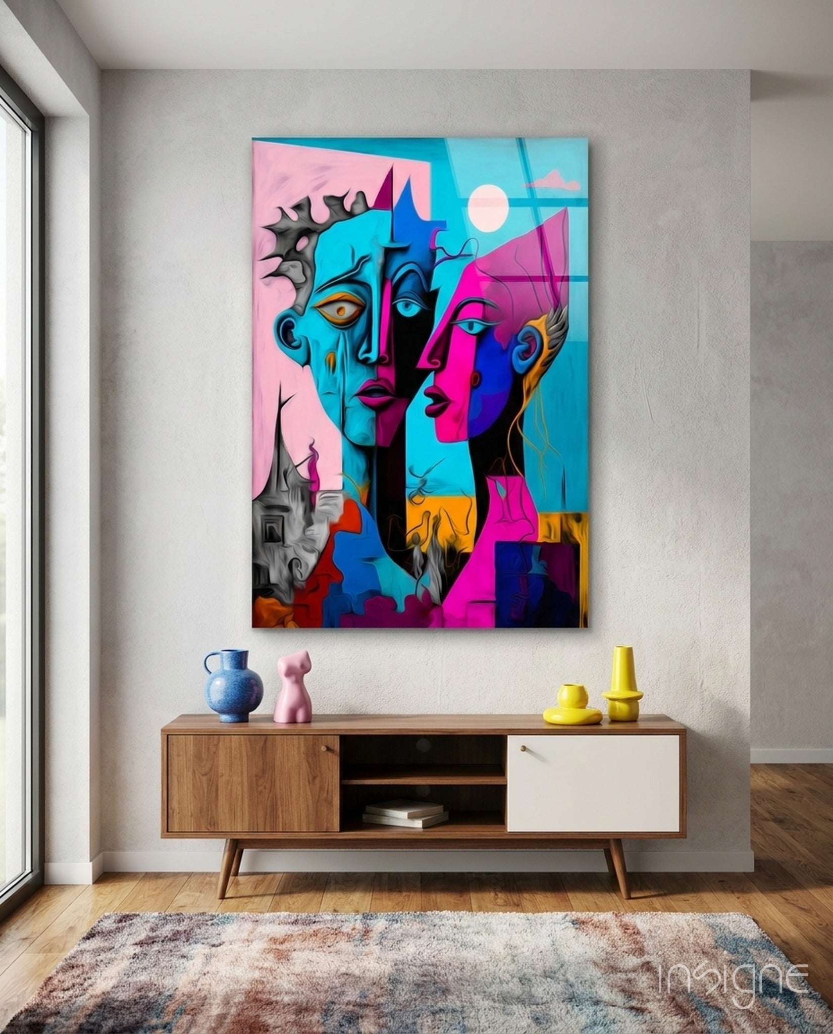 Colorful abstract faces glass wall art hanging above wooden mid-century sideboard with decorative objects and textured rug below.