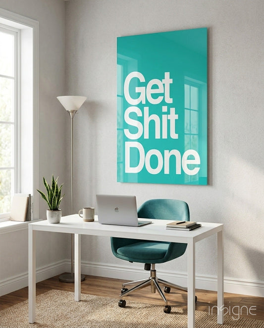 Turquoise glass wall art with white "Get Shit Done" text displayed above white desk in bright office space.