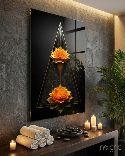 Black glass wall art featuring two golden lotus flowers in geometric triangular frame displayed above spa-themed wooden shelf with towels, stones, and candles.