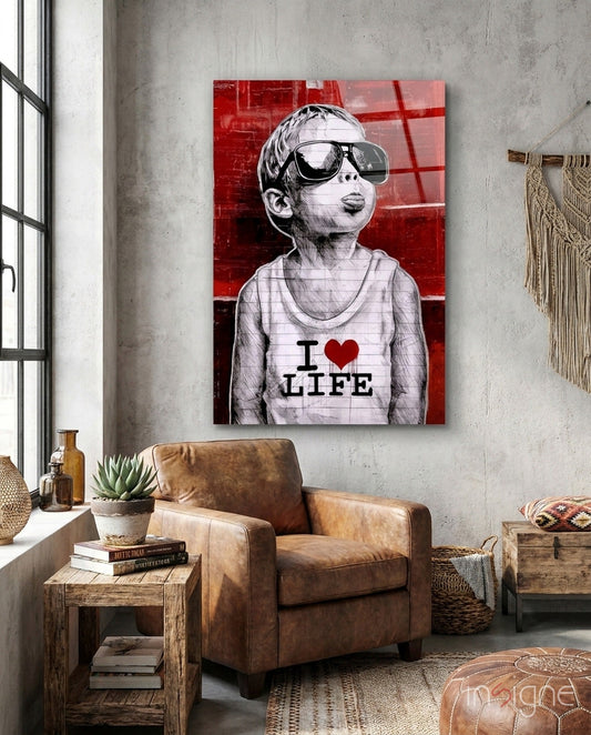 Red and white glass wall art depicting a child wearing oversized sunglasses and "I ♥ LIFE" shirt displayed above a brown leather chair.