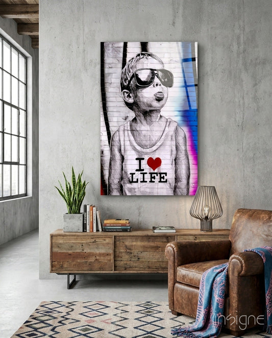 Glass wall art depicting a boy wearing oversized sunglasses and "I ♥ LIFE" shirt displayed above wooden furniture in industrial loft setting.