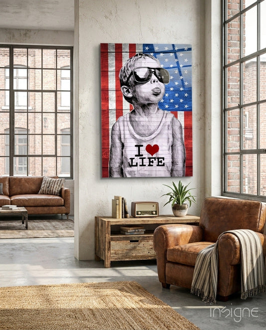 Glass wall art featuring sketch-style child wearing sunglasses and "I Love Life" shirt against American flag background, displayed in modern living room.